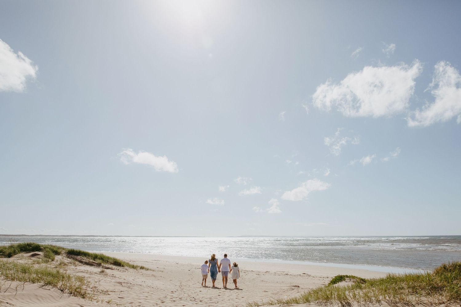 A family walking along scenic beach with dunes on a sunny day.