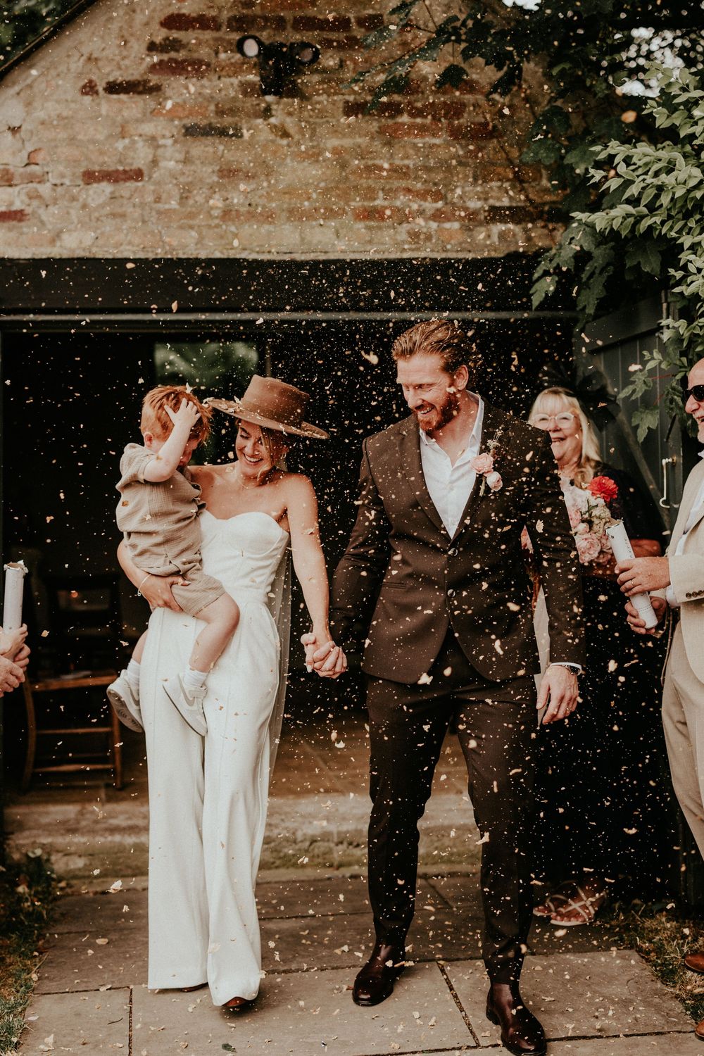 Confetti falls around a wedding couple walking down a brick path as they exit their outdoor ceremony.