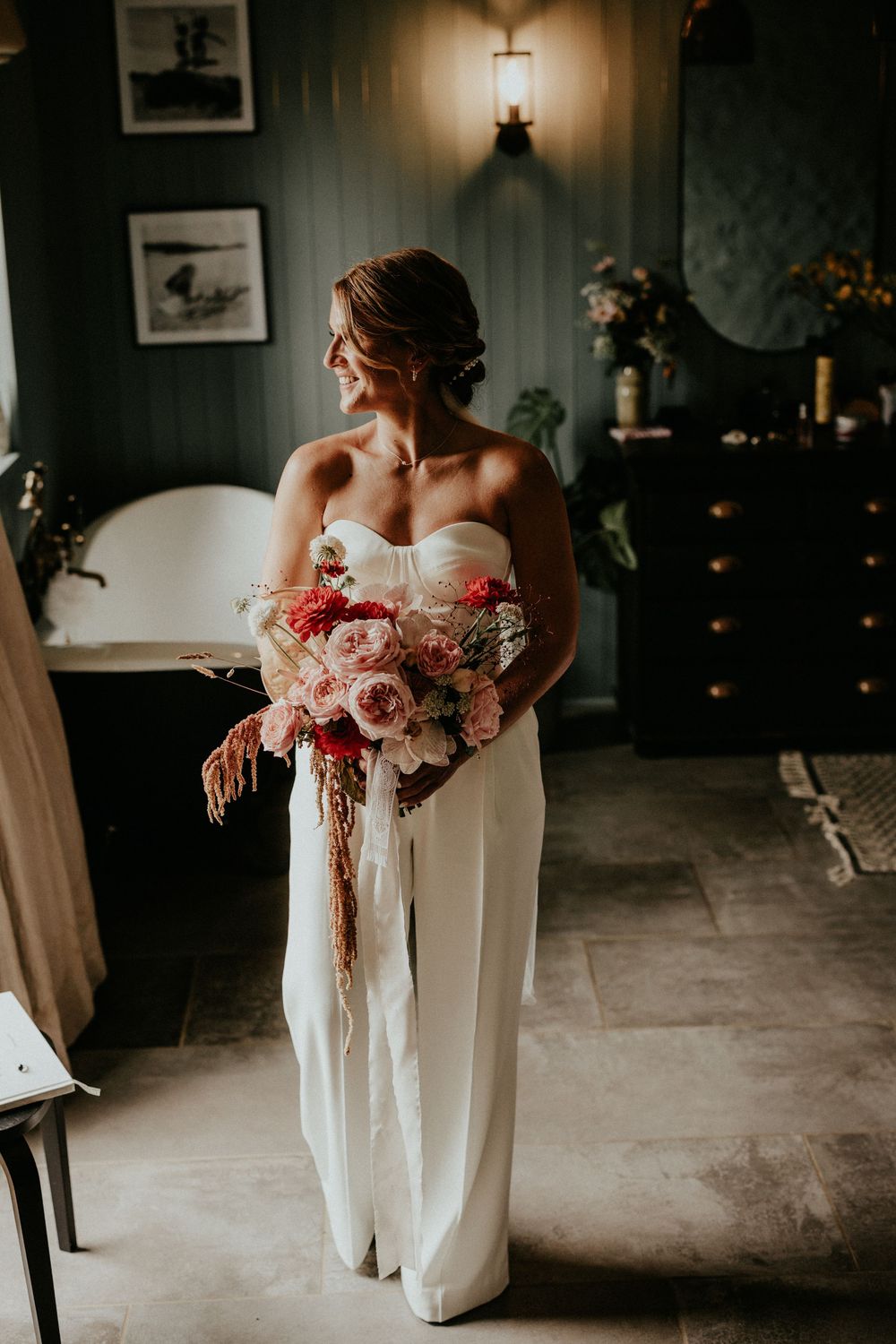 Bridesmaids in white dresses hold pink floral bouquets in a darkly lit room during a wedding photo session.