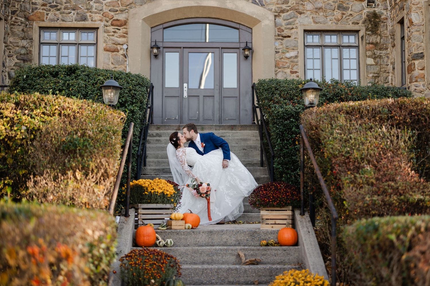 A romantic outdoor wedding scene on a green hillside with bright orange and red floral bouquet decorations.