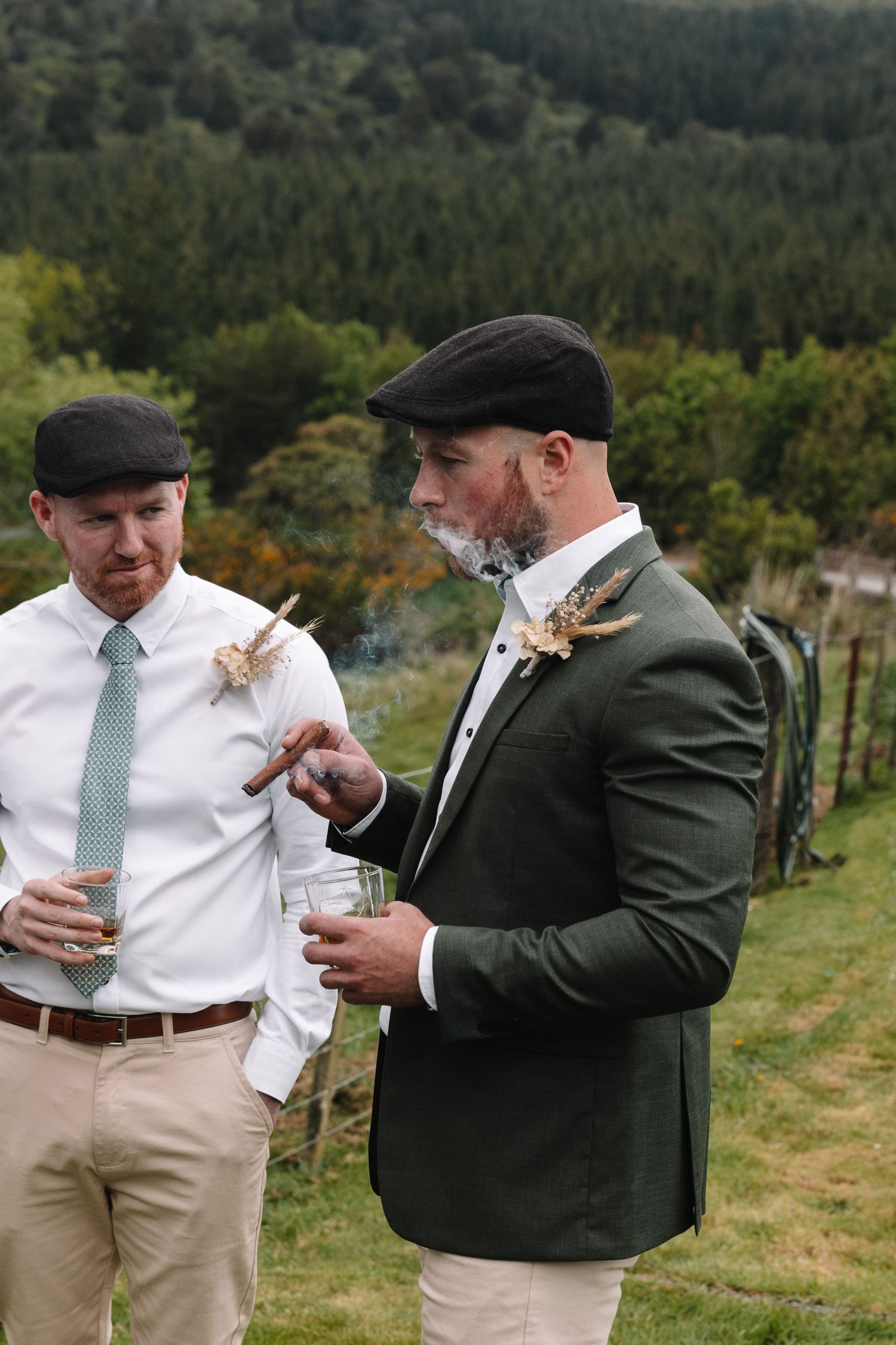 Two wedding party members share drinks and conversation on a scenic hillside.