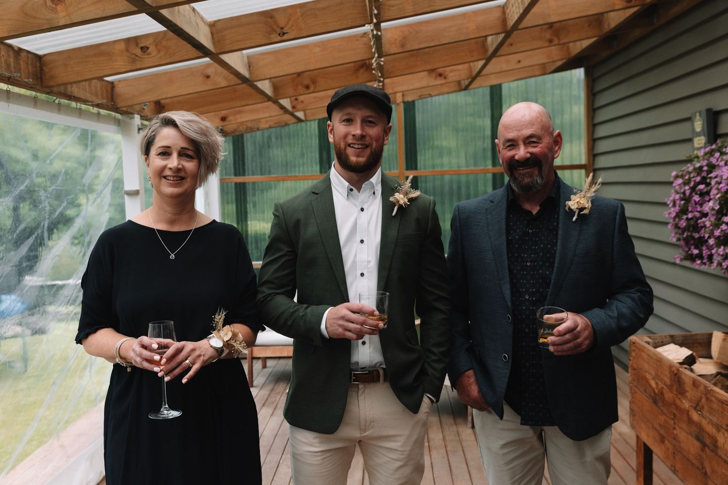 Wedding party members pose together on covered porch with drinks.