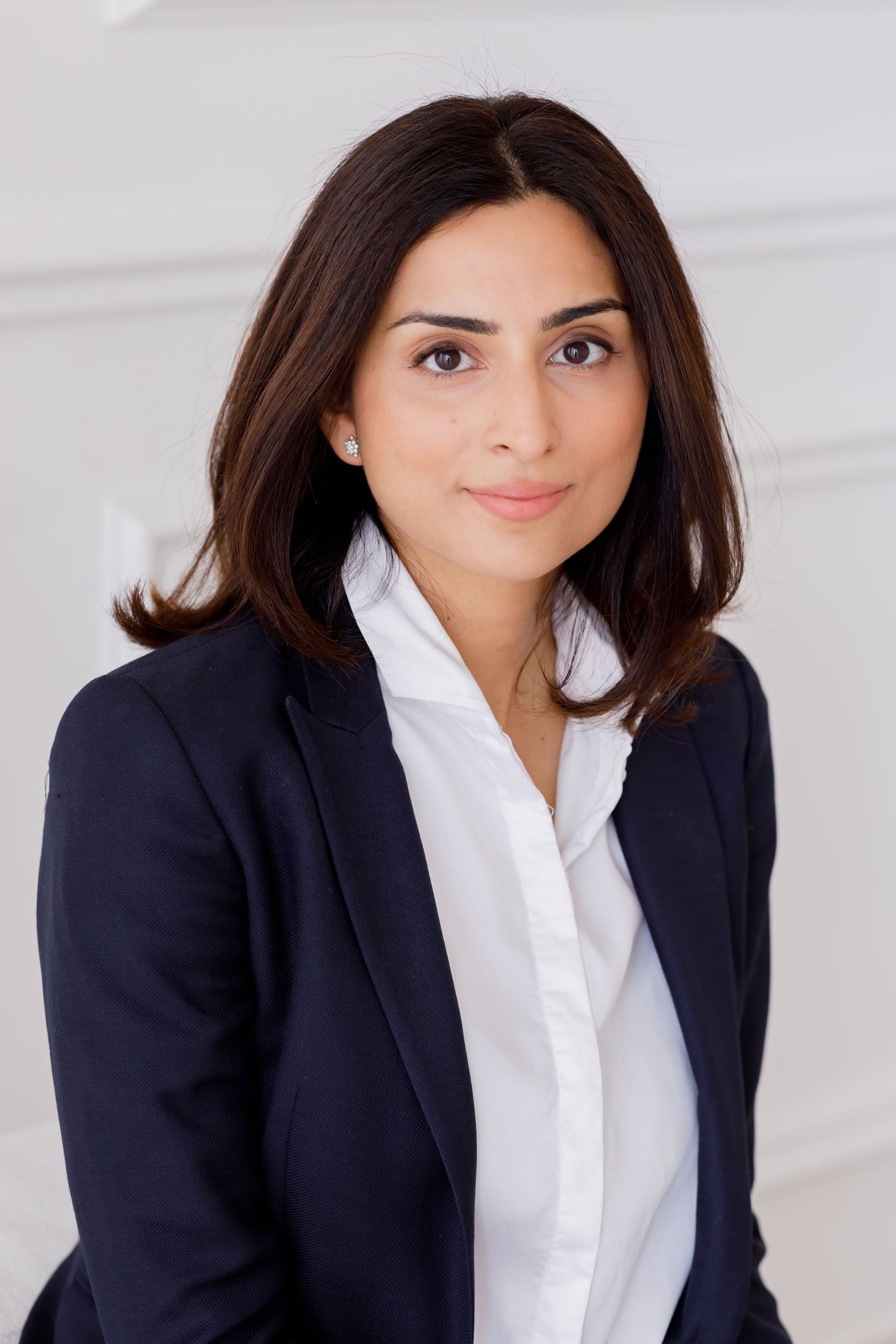 Professional business headshot of someone wearing a navy blazer and white collared shirt against light background.