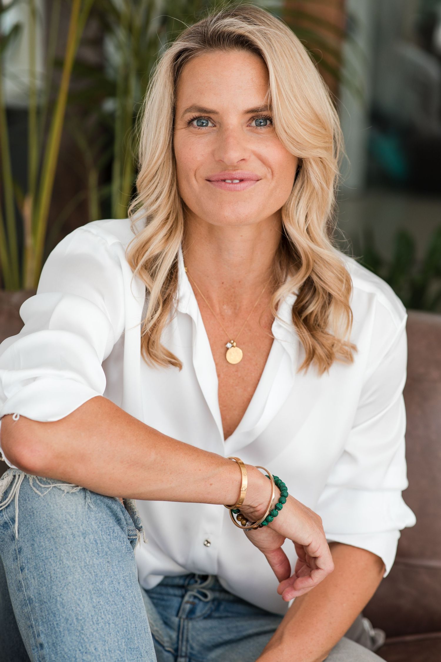 Portrait of someone wearing a classic white button-down shirt and jeans, with wavy blonde hair and delicate jewelry.