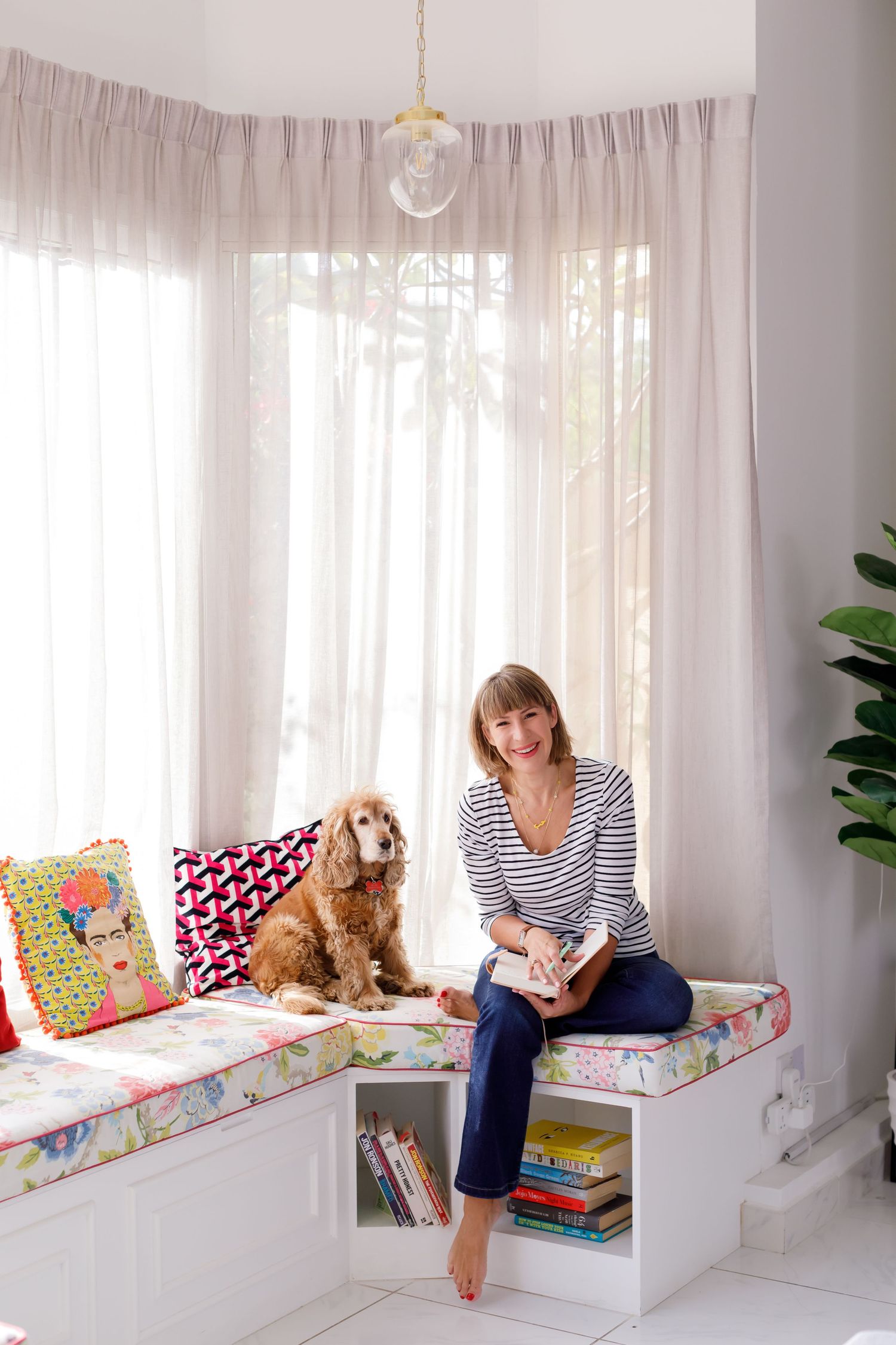 Cozy window seat nook with white built-in storage, floral cushions, and a goldendoodle dog sitting by sheer curtains.