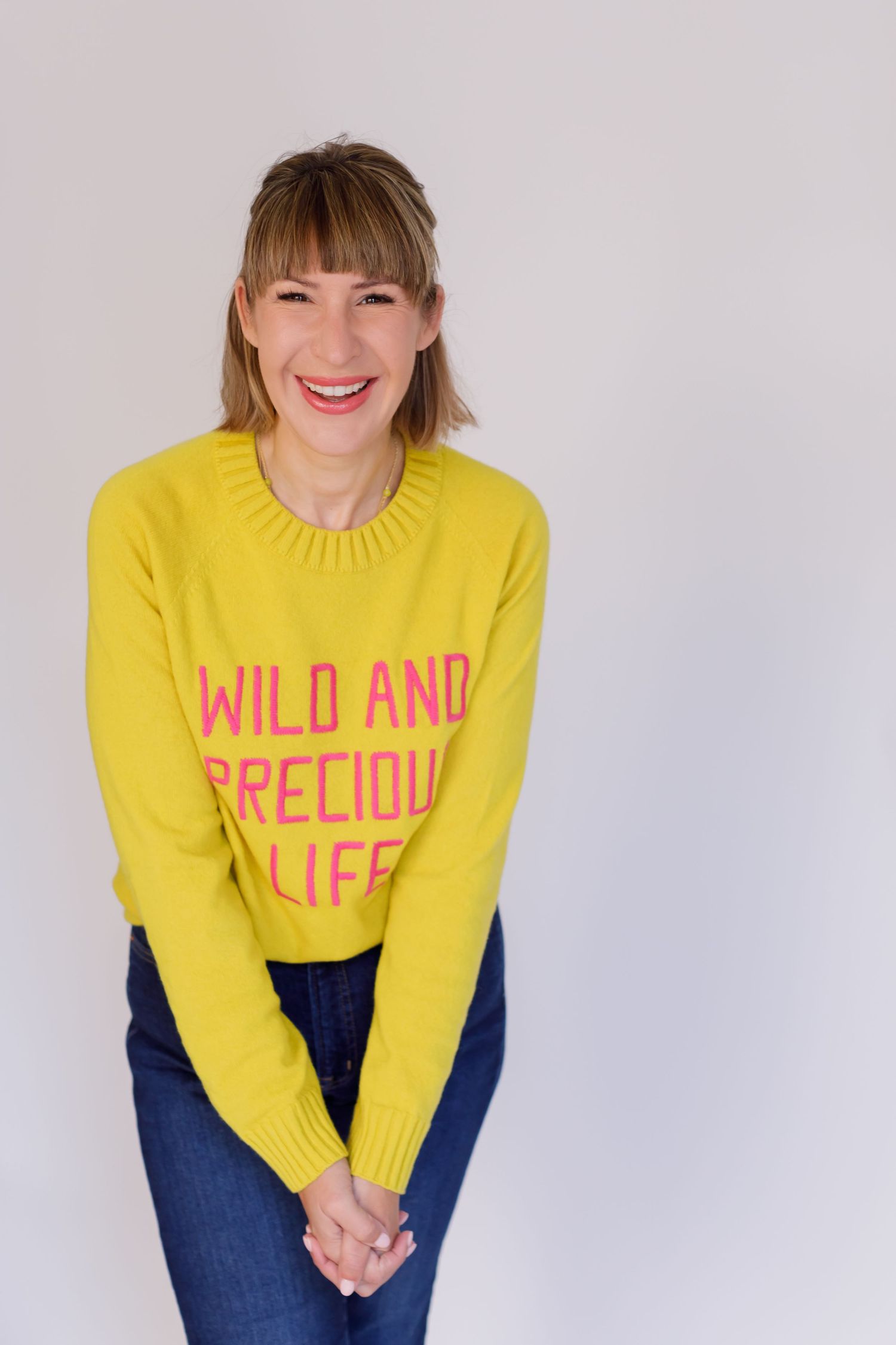 A bright yellow sweater with pink text reading 'Wild and Precious Life' styled with blue jeans against a light background.