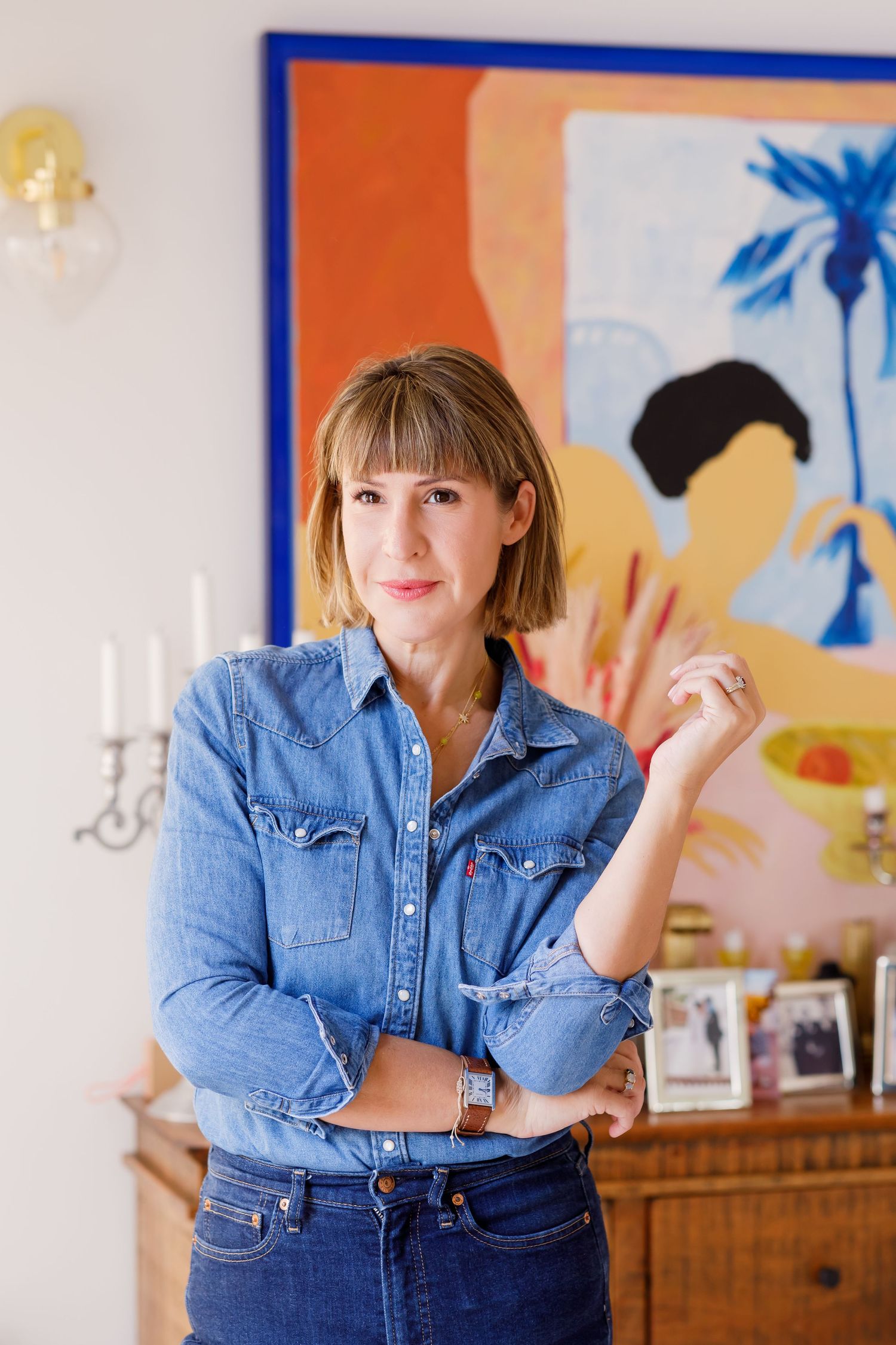 Person wearing denim on denim outfit stands in casual pose against wall with colorful artwork.