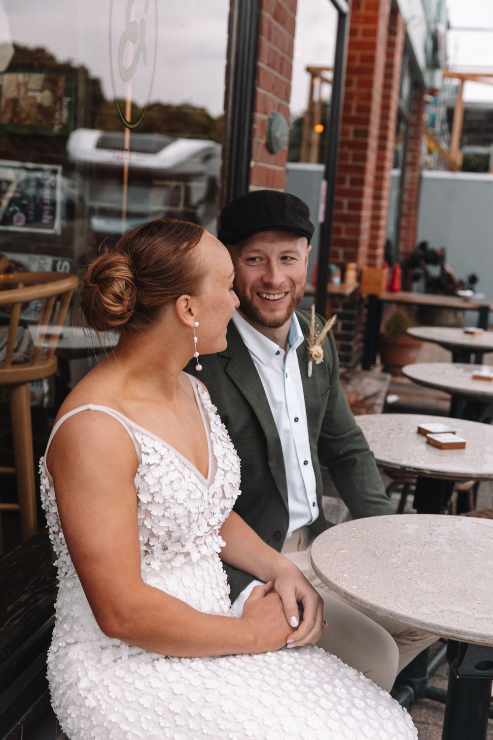 A couple shares an intimate moment at a cafe table with brick walls and window reflections.