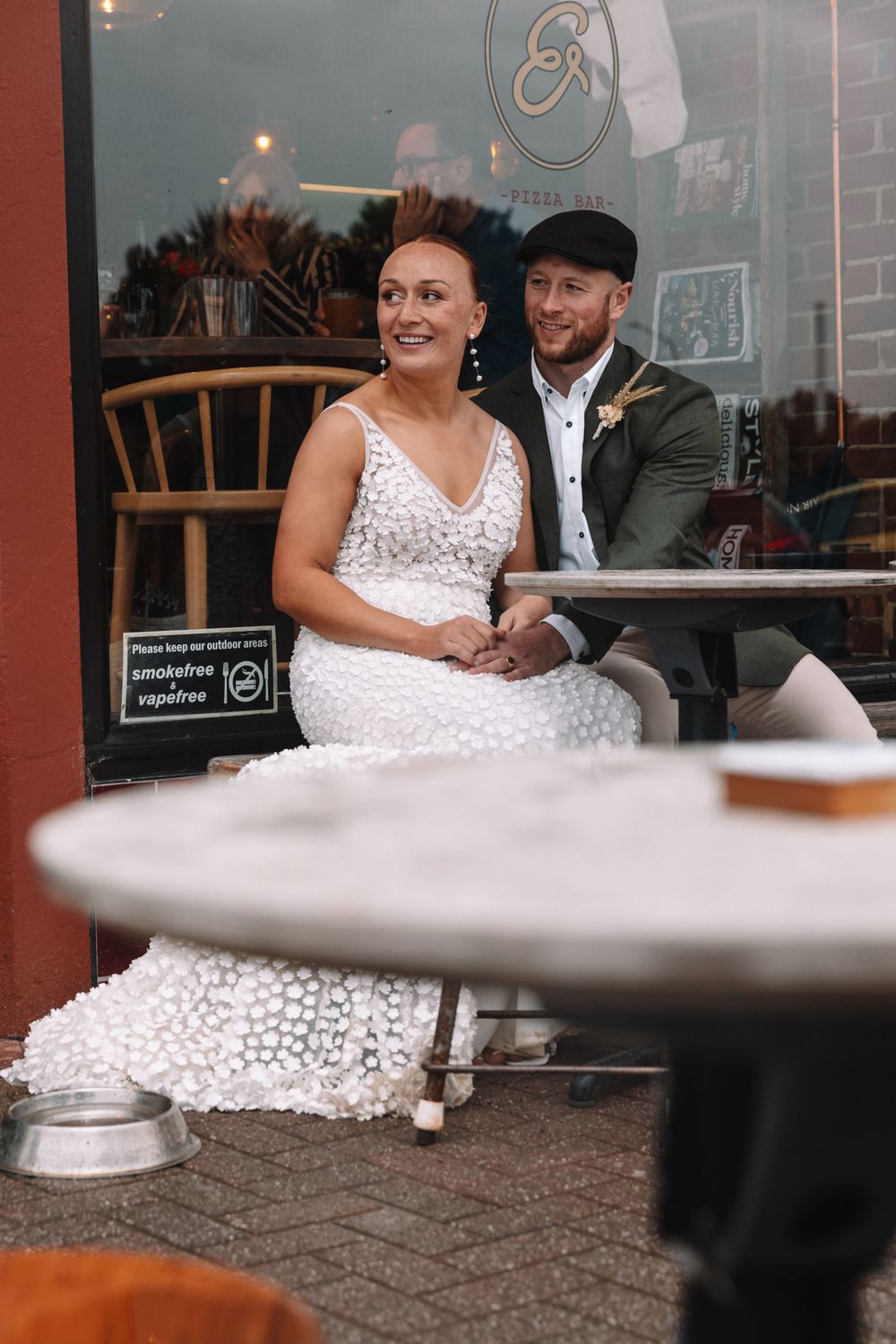 A couple sits by a cafe window with vintage decor and outdoor tables visible.