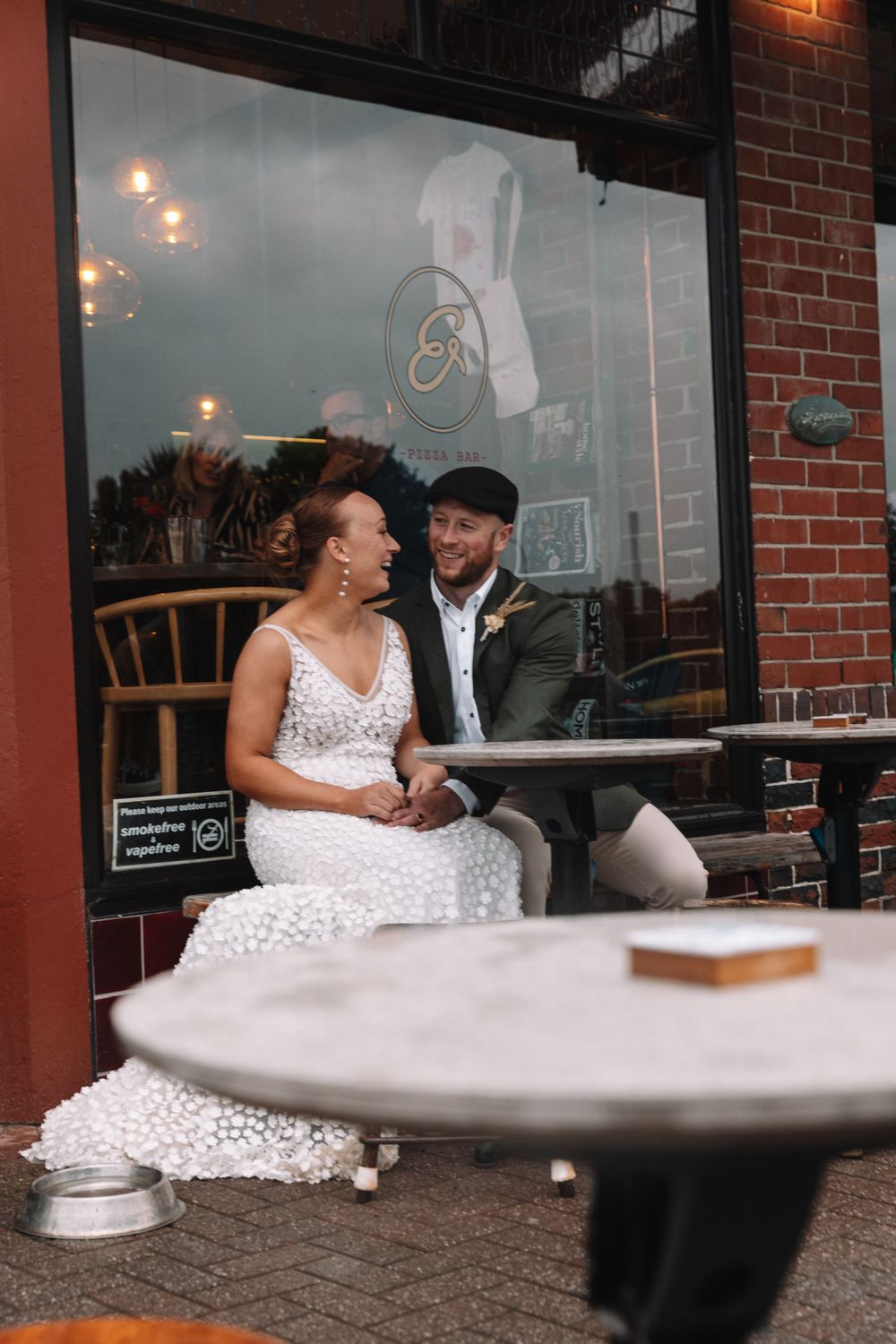A couple shares laughter at an outdoor cafe with brick walls and round tables.