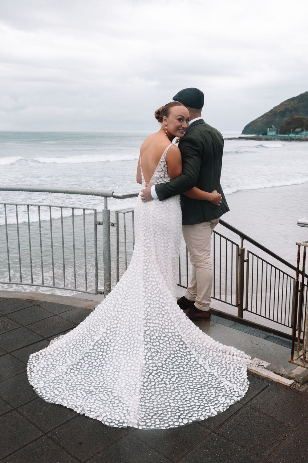 Wedding couple sharing a tender moment overlooking the ocean on a cloudy day.
