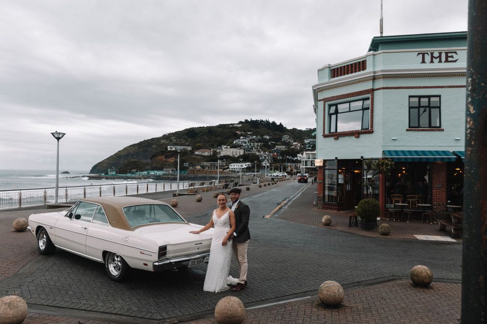 A classic white vintage car parked near a coastal building with round stone barriers.