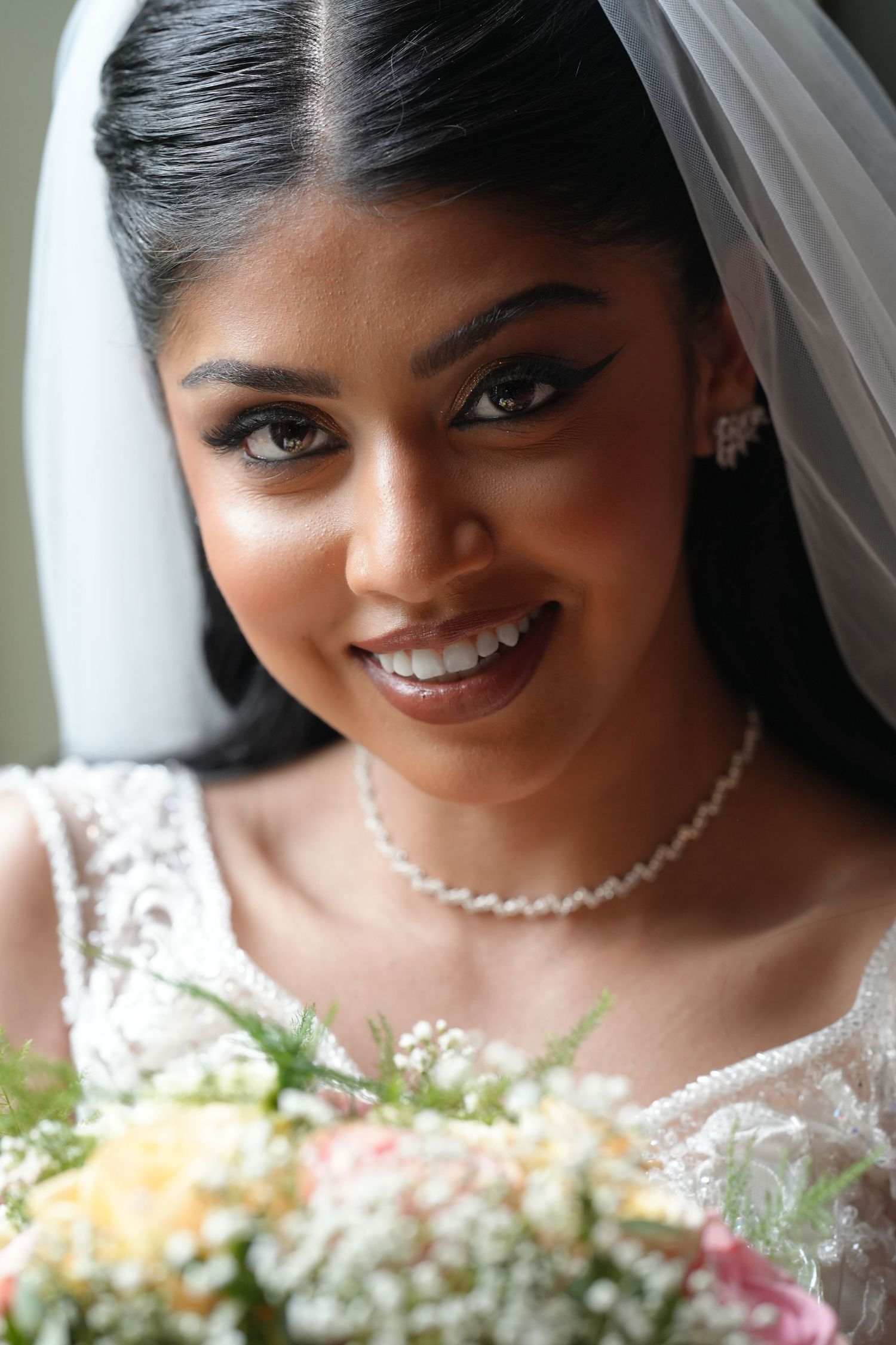 Bridal portrait showing radiant smile, pearl necklace and white veil against light background.