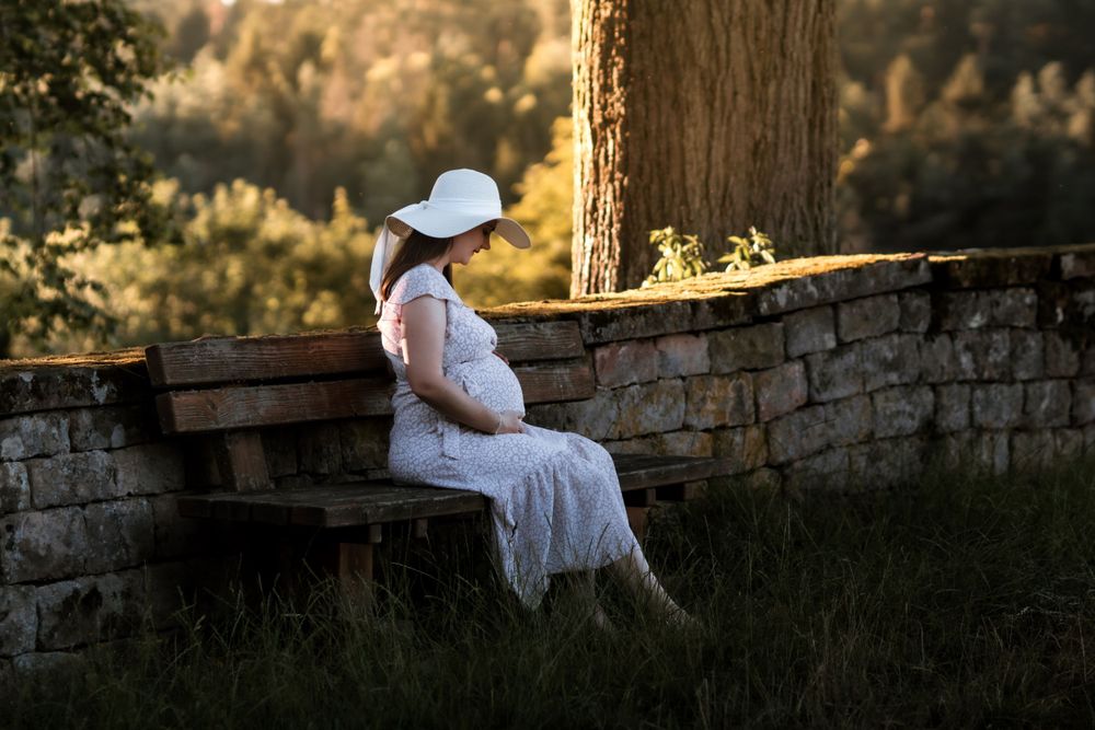 Schwangere Frau in einem fließenden Kleid, fotografiert vor einer malerischen Waldkulisse in Trippstadt.