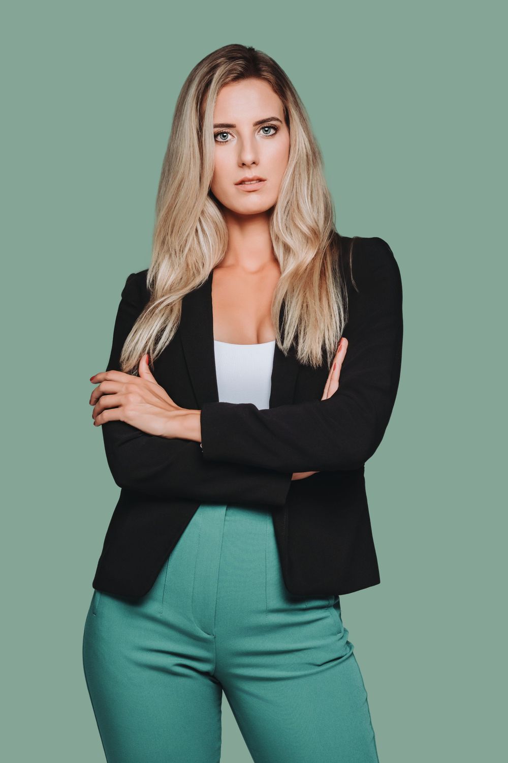 Stylish business outfit with black blazer and green pants against mint green backdrop.