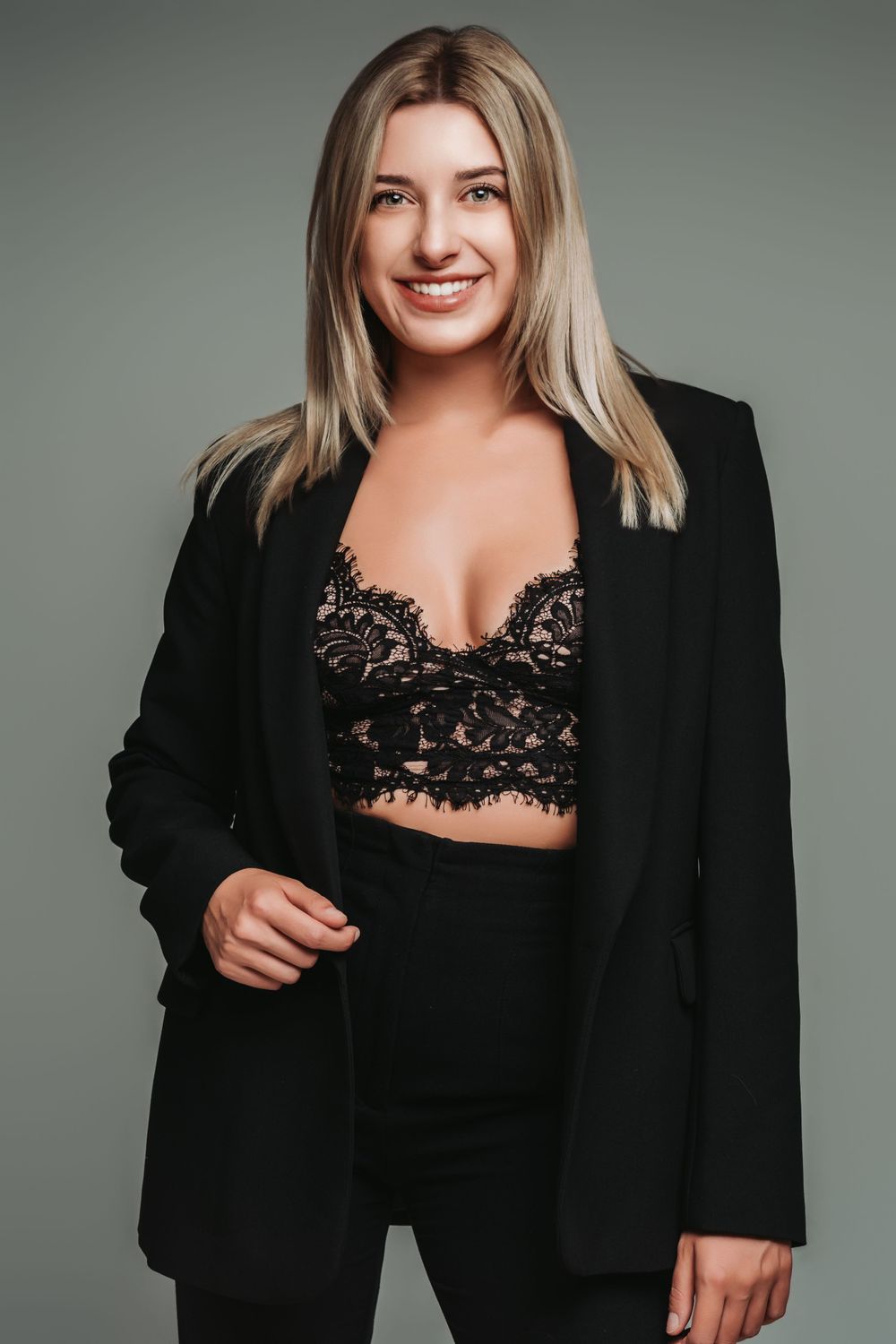 Modern fashion portrait featuring black blazer and lace top against grey background.