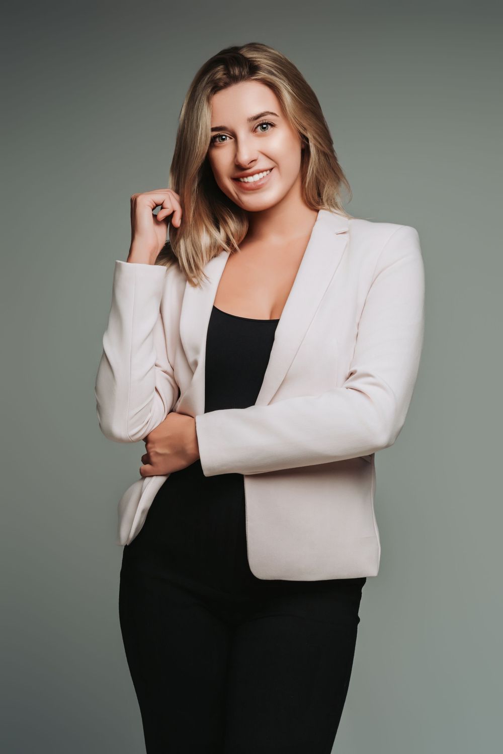Professional headshot featuring cream blazer and black top against grey background.