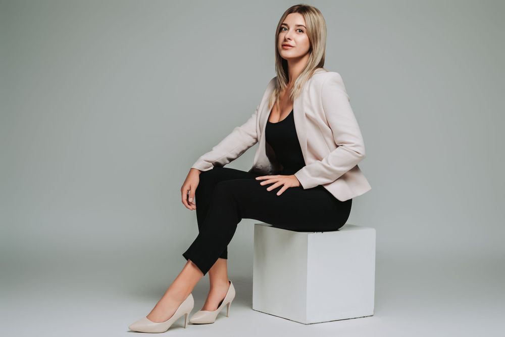 Professional studio shot showcasing cream blazer and black outfit while seated on white cube.