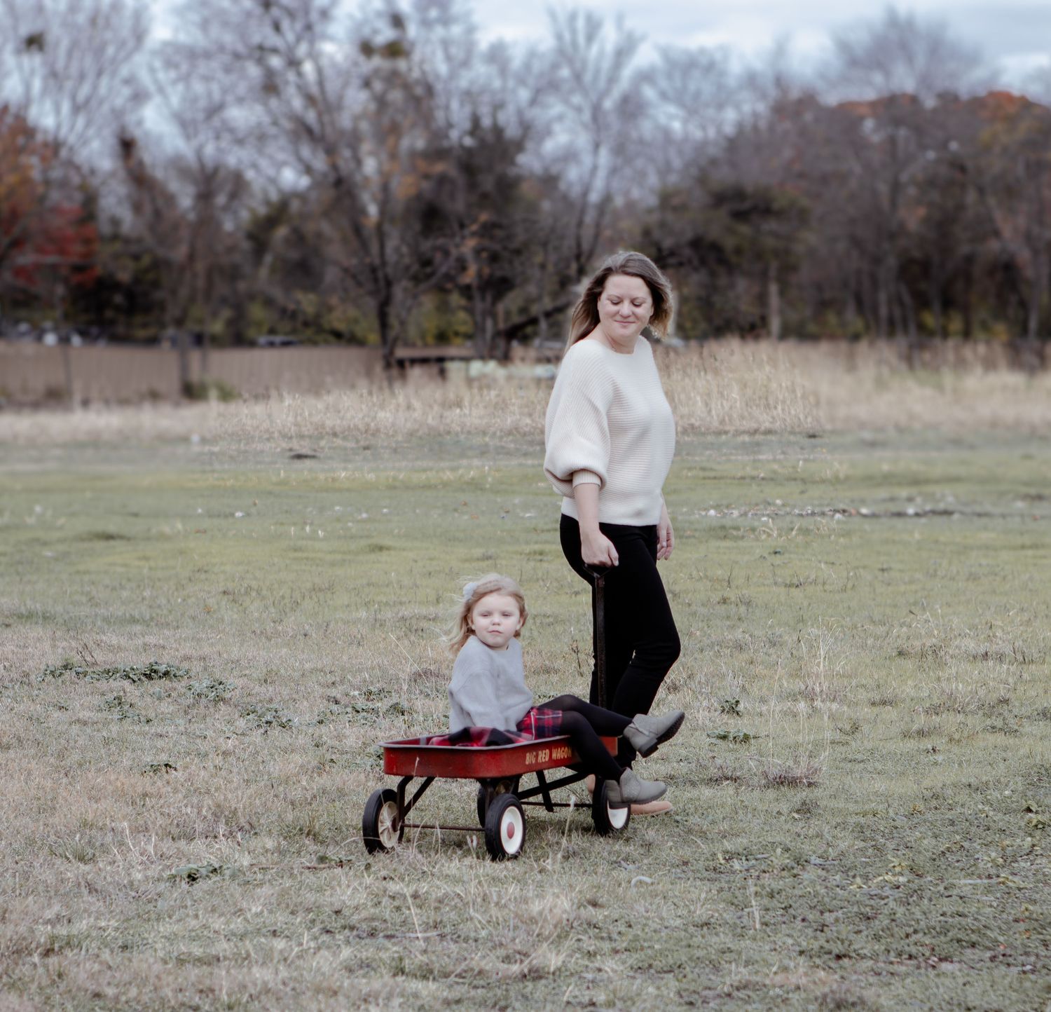 A cheerful outdoor scene with people and a red wagon in an open field during fall.