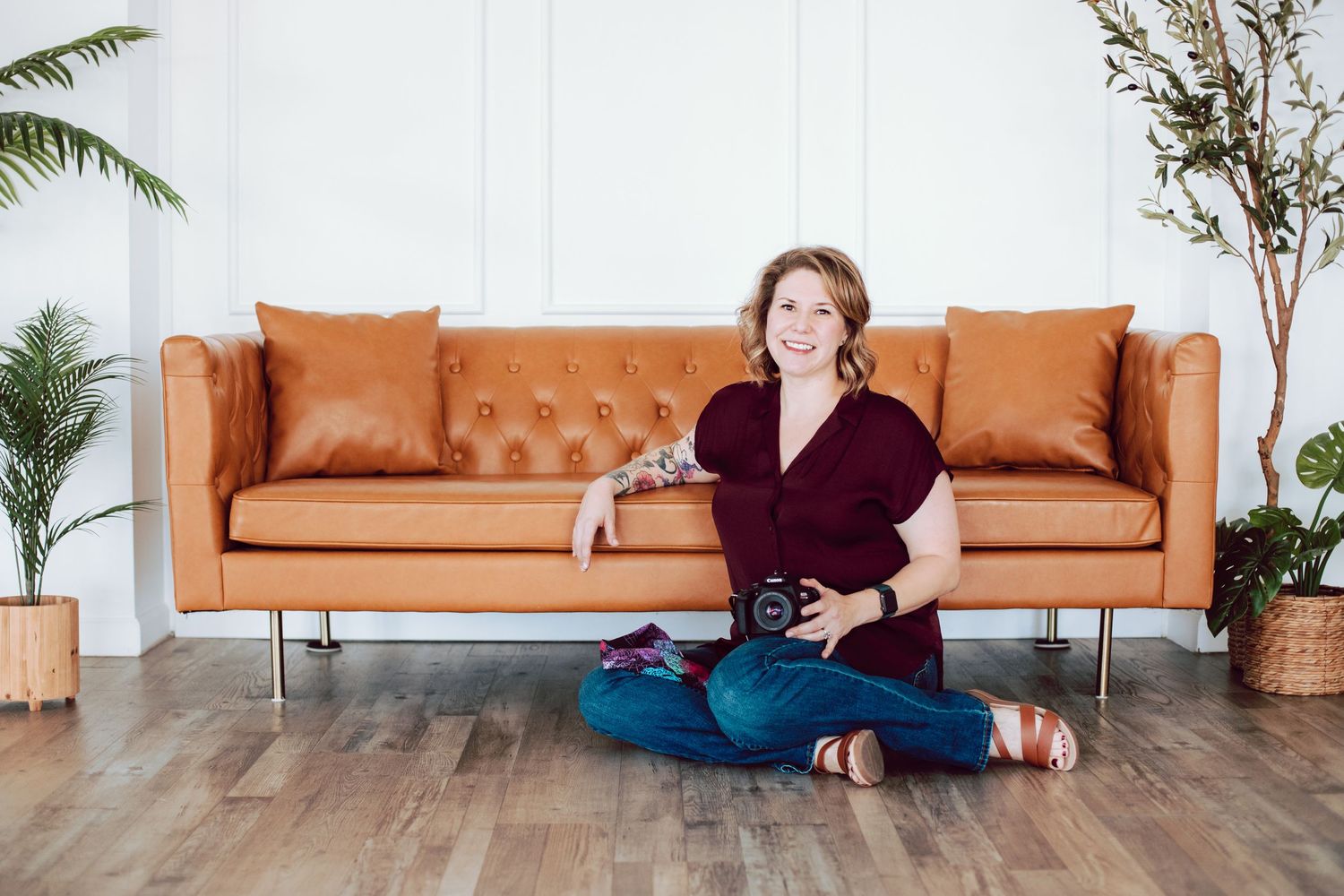 Person sitting cross-legged on floor next to modern orange leather sofa with plants.