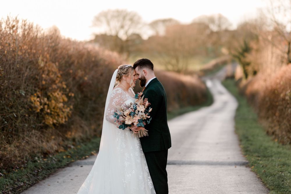 Newlyweds share an intimate moment on a country path surrounded by autumn foliage.