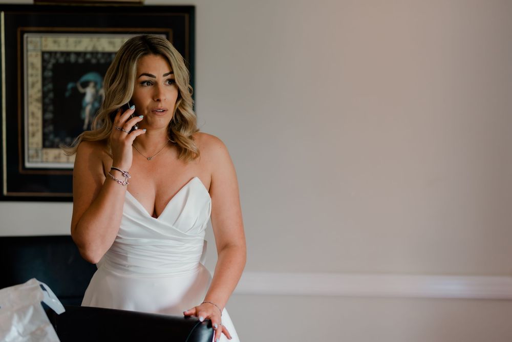Elegant figure in white formal dress leans thoughtfully against wall during wedding preparations.