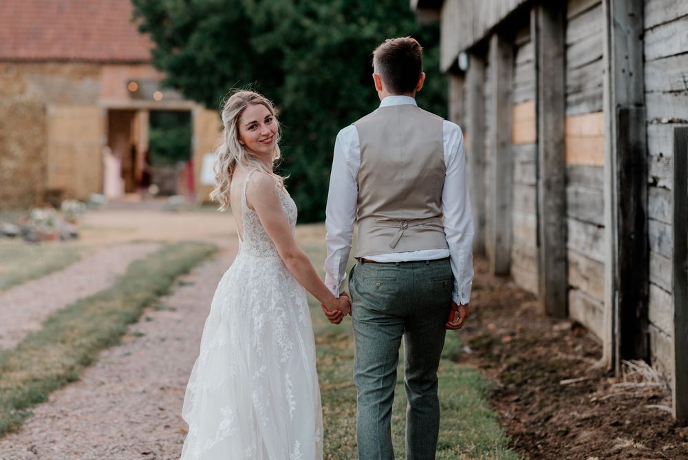 A bride and groom share a tender moment together on a rustic dirt path beside a wooden barn wall.