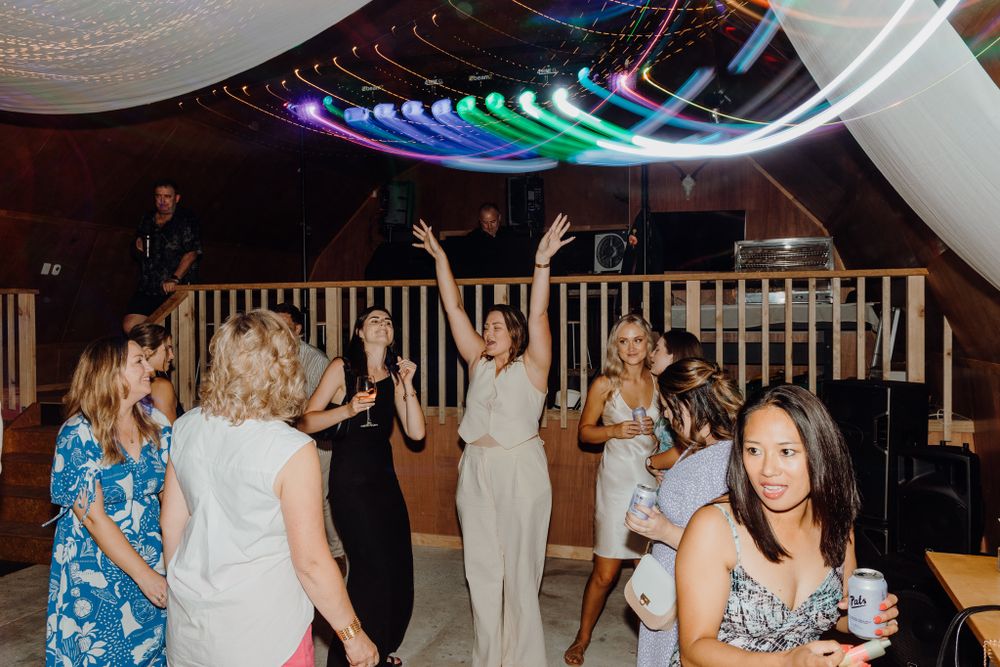 Wedding guests dancing under colorful neon lights and white draping at indoor reception.