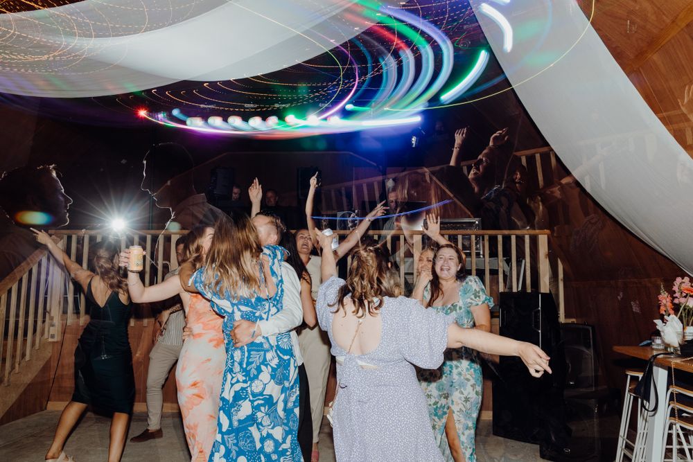 Wedding reception dance party with colorful LED lights and white fabric ceiling decorations.