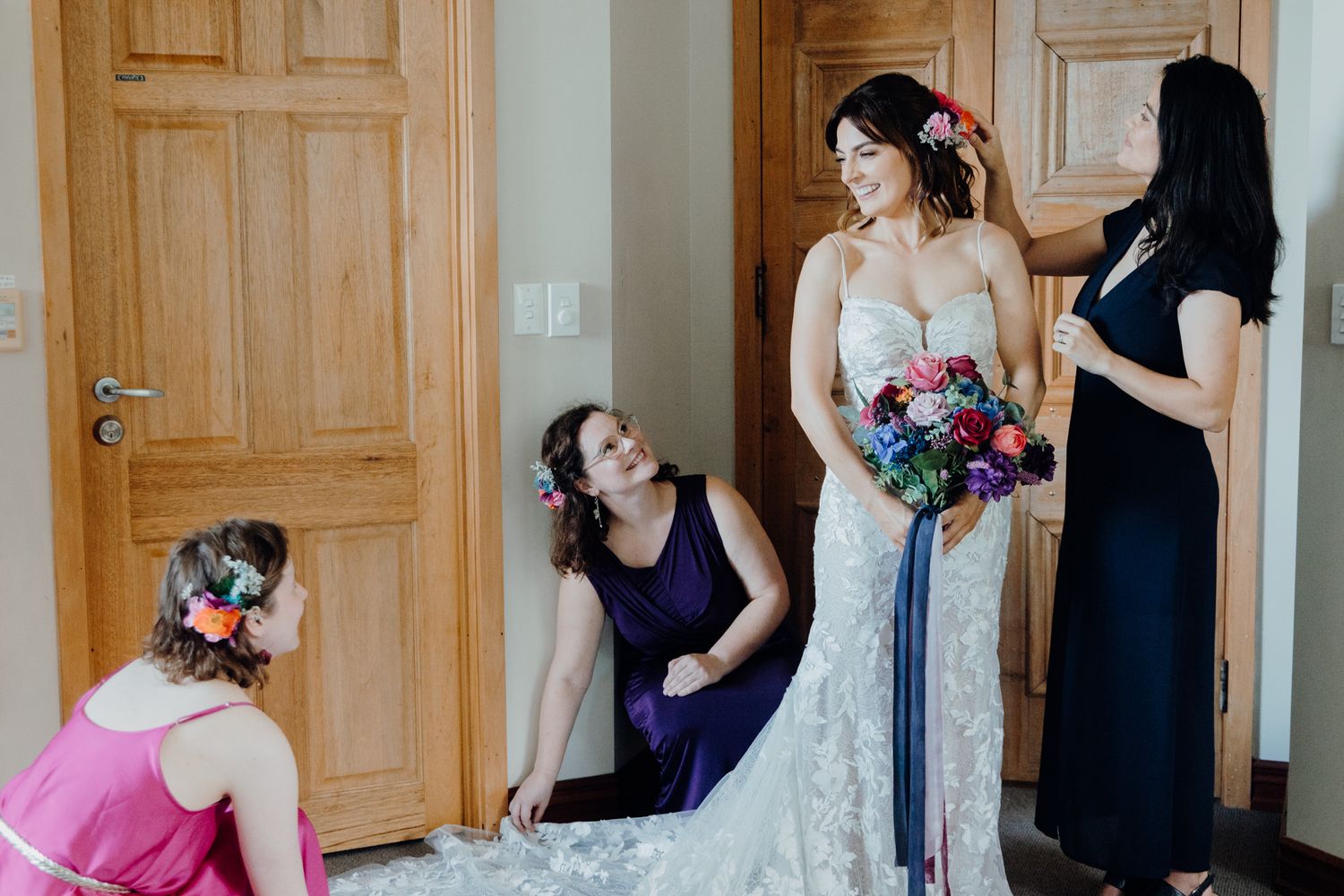 A bridal party helps adjust a wedding dress in front of wooden doors.