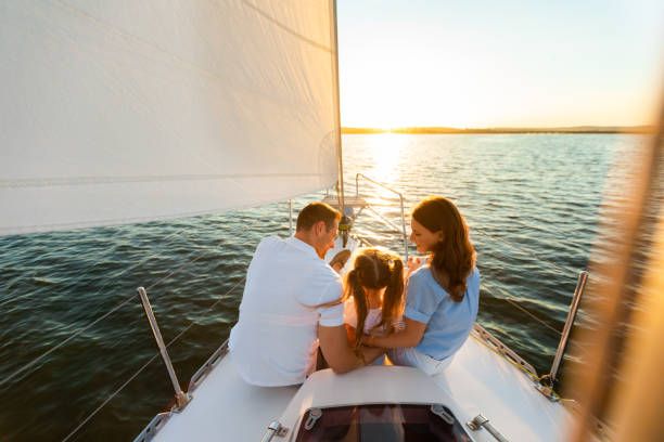 Family enjoying a sunset sail together on calm waters with white sails and golden light.