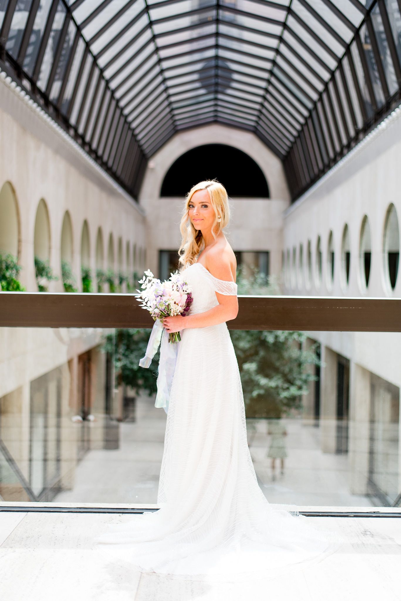 blonde bride smirking in atrium of The Center Cincinnati with pink and purple wedding flowers