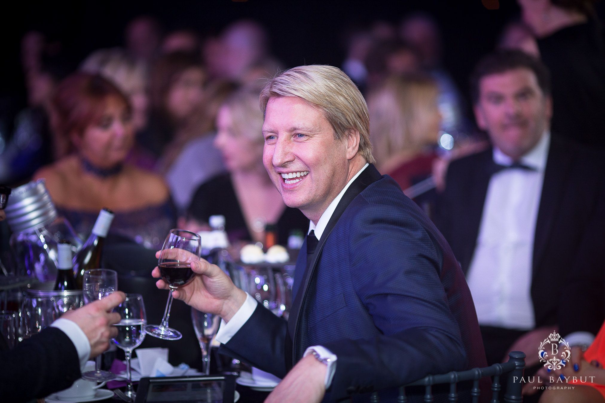 Smiling male guest sat a a table and holding a glass of wine during a charity ball event in Manchester