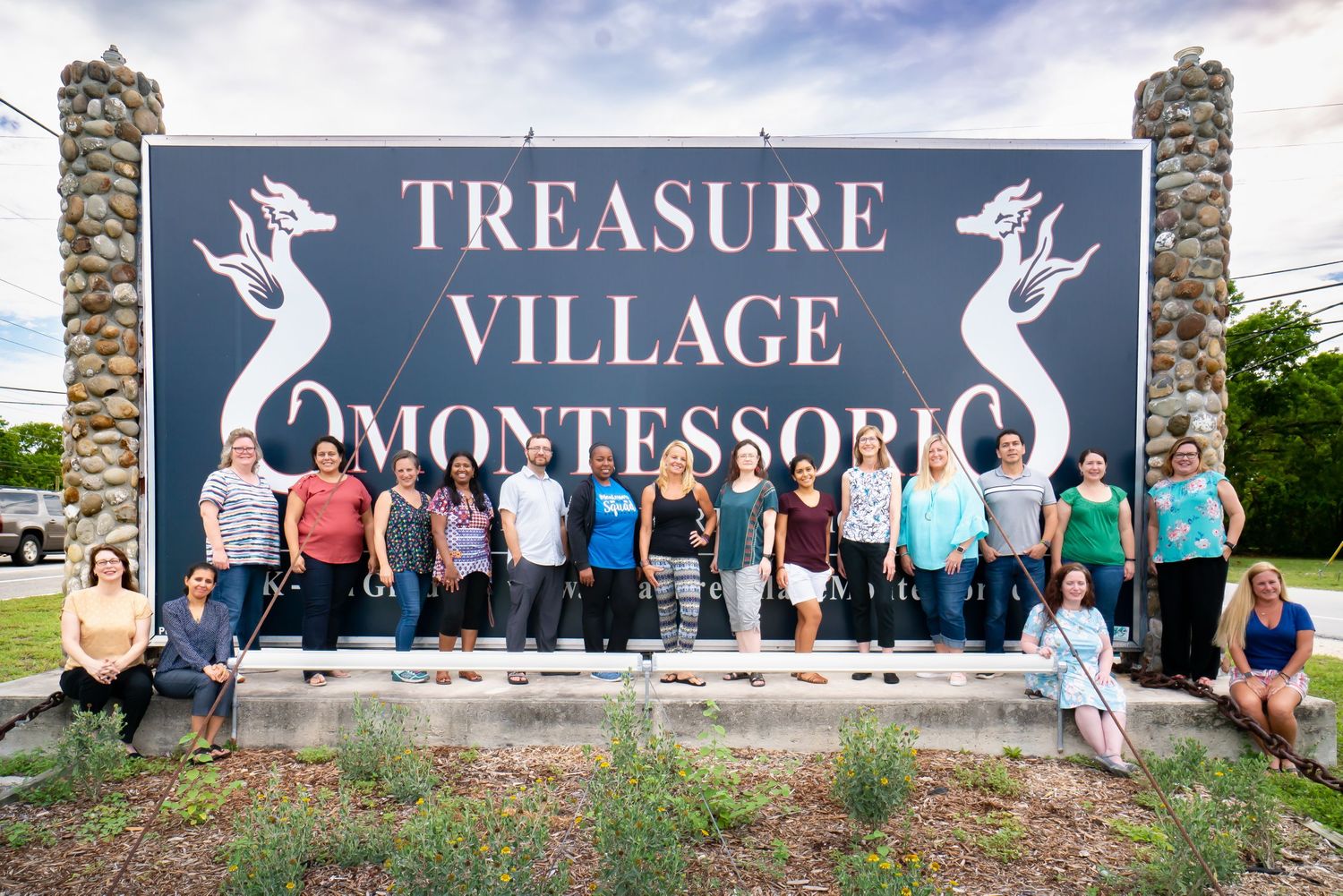 Stone wall with multiple signs reading 'Treasure Village Montessori' in white lettering.