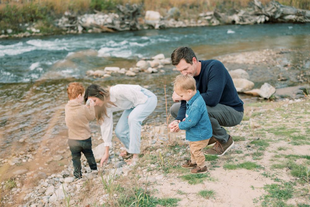 Family exploring together by a rushing river on a sunny day.