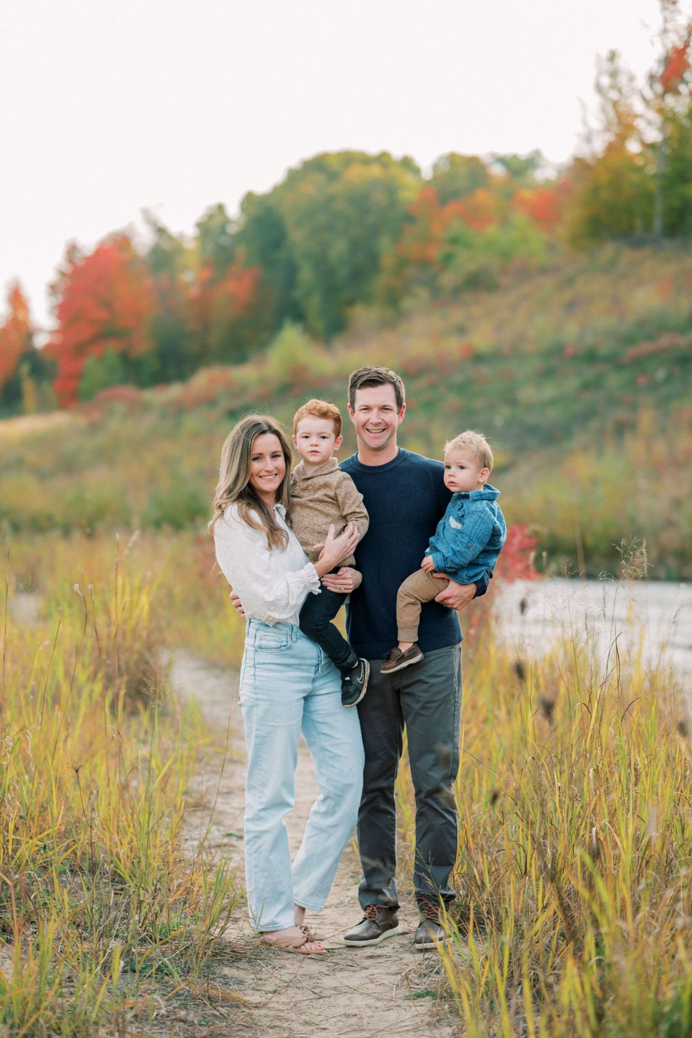 Family of four standing together on nature trail during autumn season.