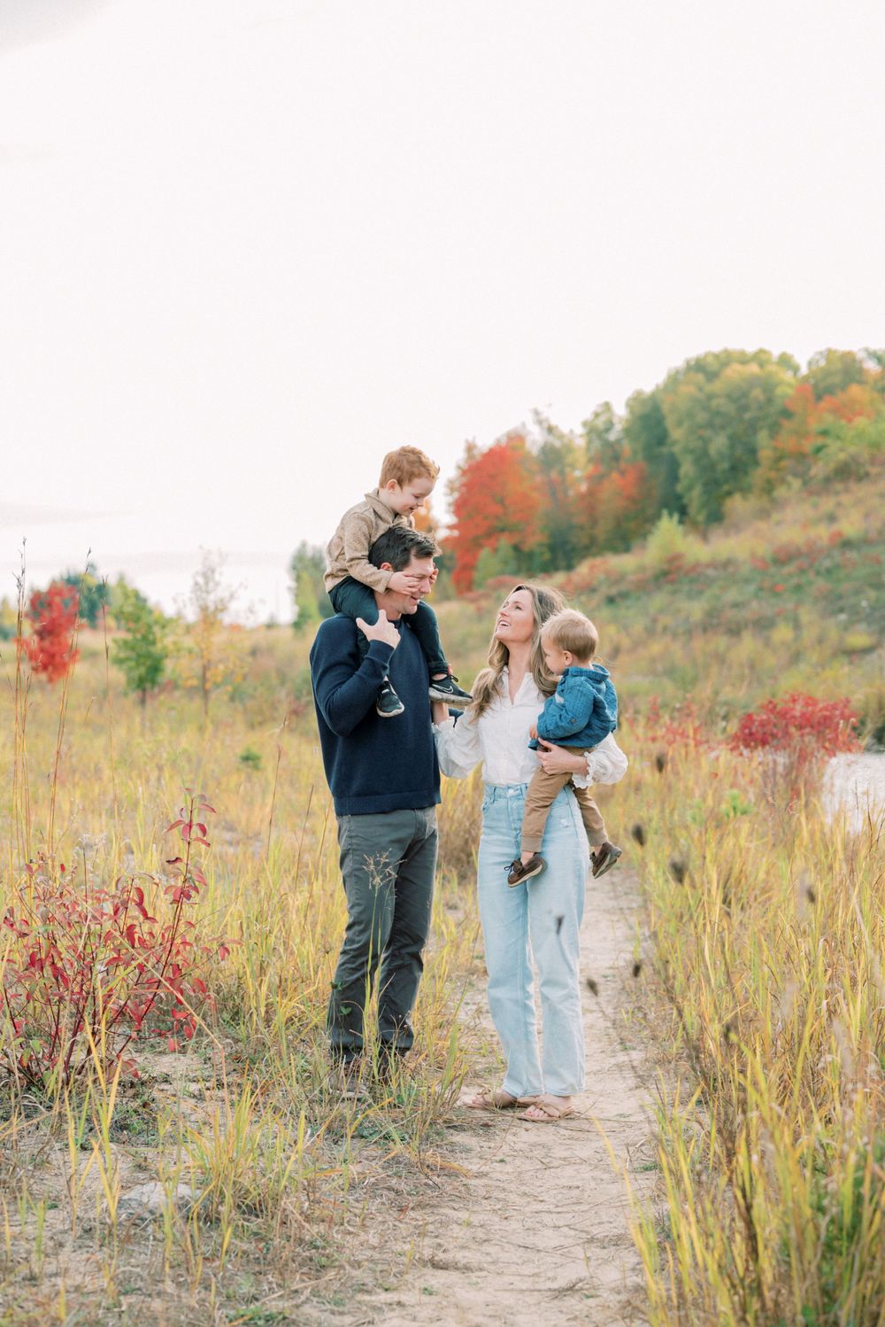 A loving family moment captured on a dirt trail surrounded by autumn foliage and tall grass.