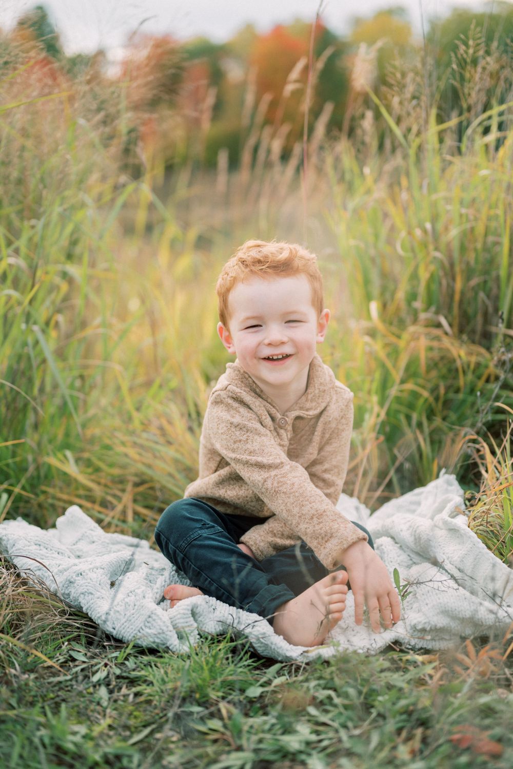 A joyful moment captured in tall grass with a beige sweater and blanket on an autumn day.