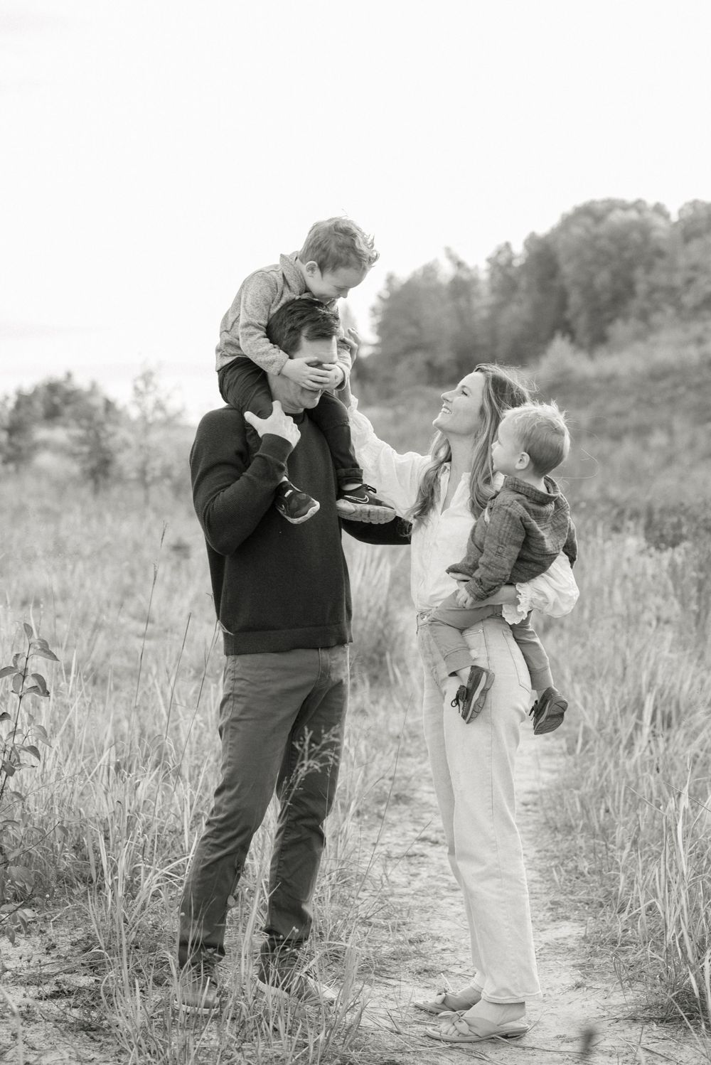 Black and white photo of family playing and laughing together in tall grass.