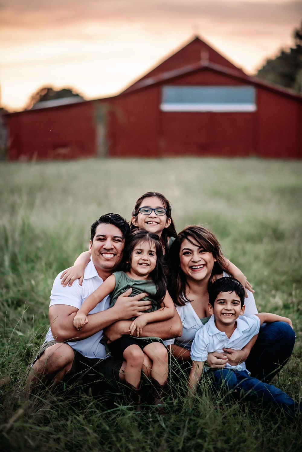 photo of a family sitting in a grassy field in front of a red barn