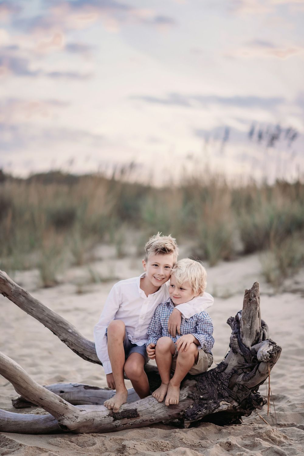 Photo of two boys sitting on a driftwood branch on the beach