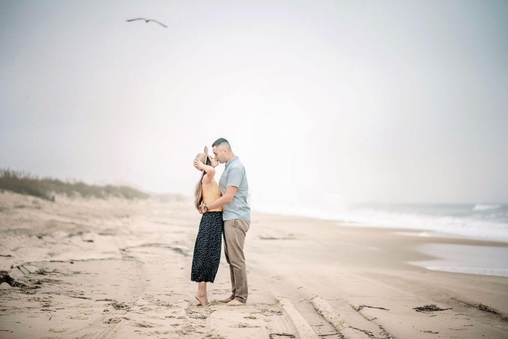 a photo of a man and woman kissing on the beach while the woman holds her hat