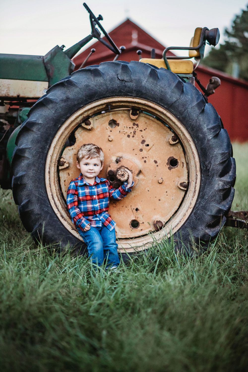 photo of a toddler boy standing in front of a tire on a John Deere Tractor