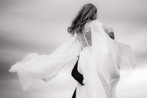 A flowing white wedding dress billows dramatically in black and white photography.