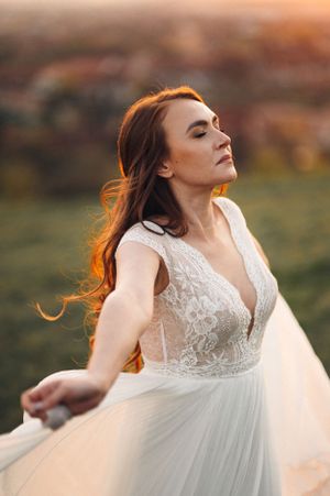 A bride in a lace wedding gown poses at sunset with flowing fabric and golden light.