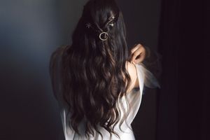 Back view of long dark wavy hair with decorative hair accessory against dark background.