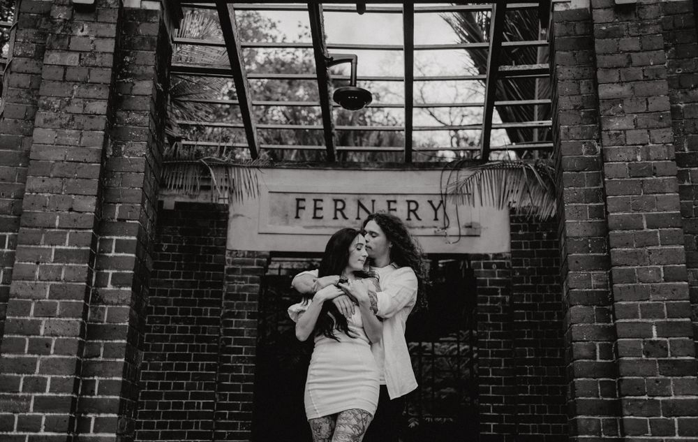 Black and white photo of a couple standing beneath the Fernery sign on a brick building.