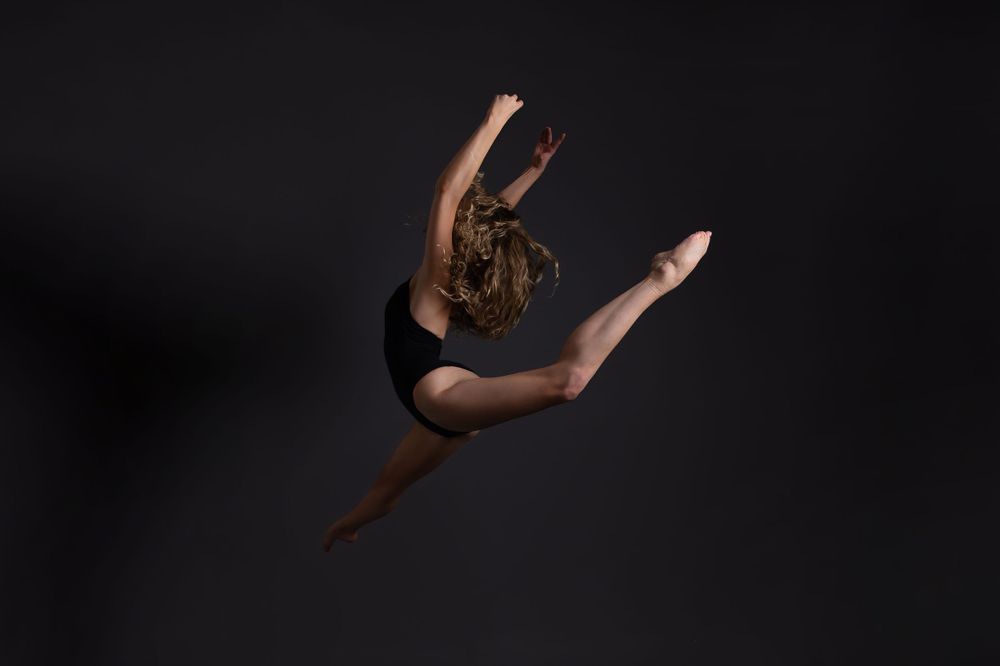 female dancer in black leotard leaping in the air