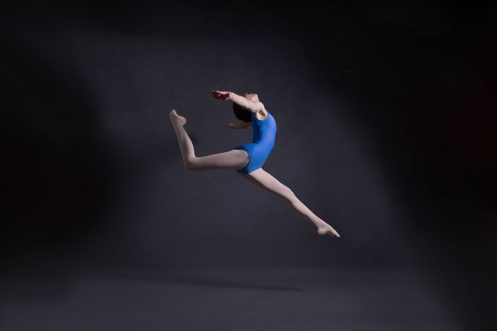 female teen dancer in blue leotard jumping in air