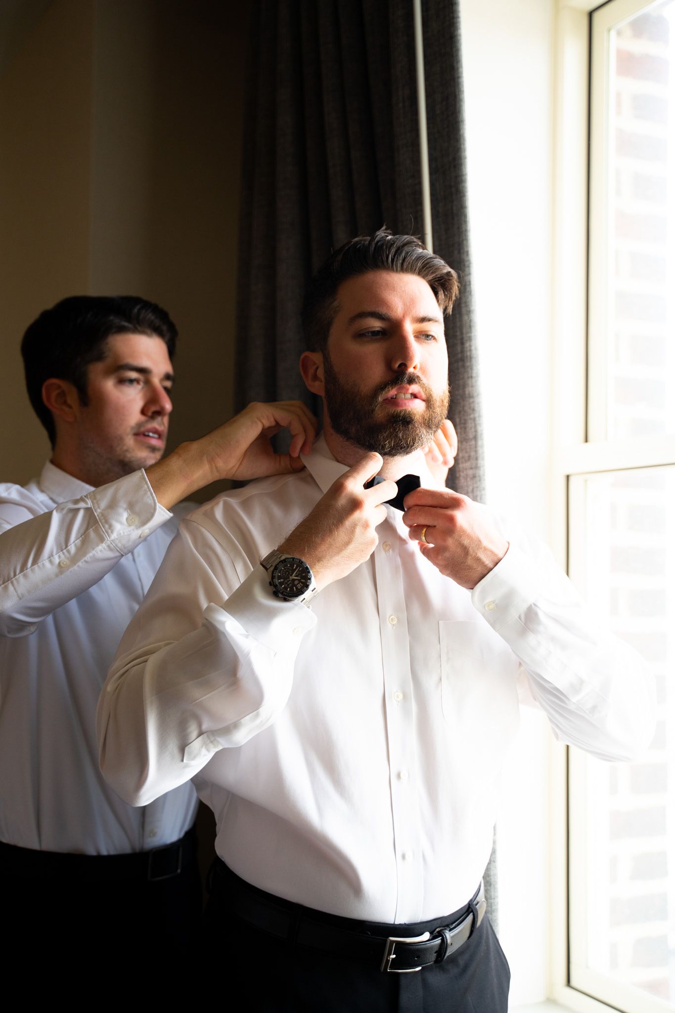 brunette groom fixing bowtie near a window for Chicago wedding